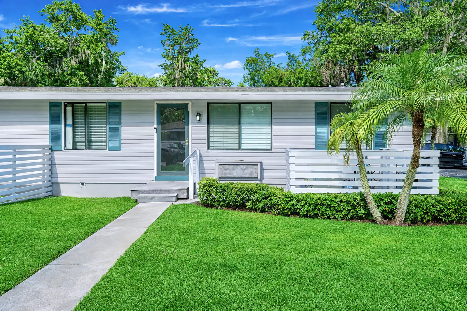 Single-story bungalow with teal shutters, a private walkway, and fenced patio.
