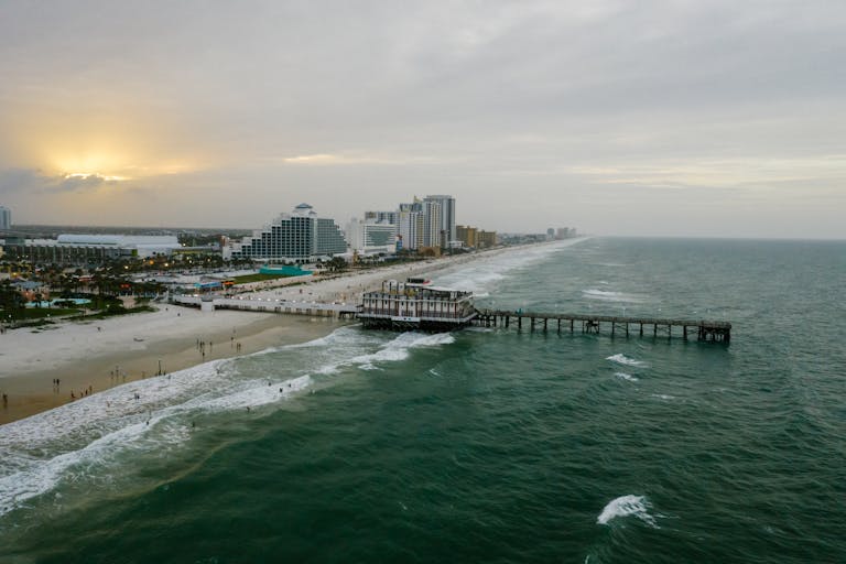 A stunning aerial view of Daytona Beach's pier and coastline at sunset with vibrant ocean waves.